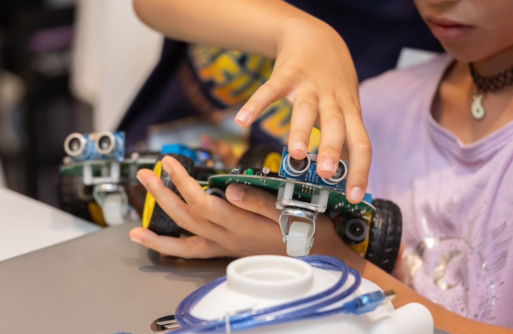 Manos de una niña ensamblando un robot con sensores en un taller STEAM
