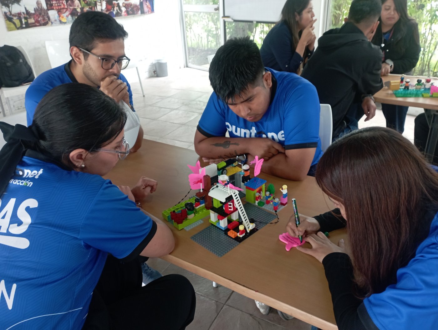 Equipo de voluntarios de PuntoNet construye un modelo con bloques y toma notas durante el taller